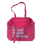 Pink tote bag with 'the Bondi Beach tote bag' text in aqua blue