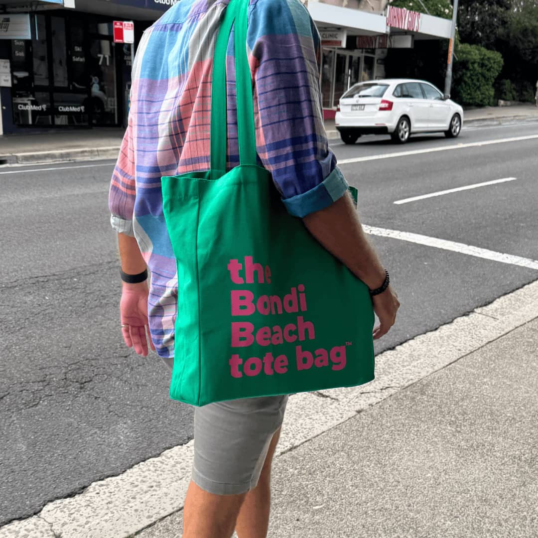 Person holding green canvas Bondi Beach tote bag with zip pocket on street.