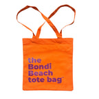 The Bondi Beach tote bag Little Bondi in orange with purple print flatlay closed showing slim durable canvas
