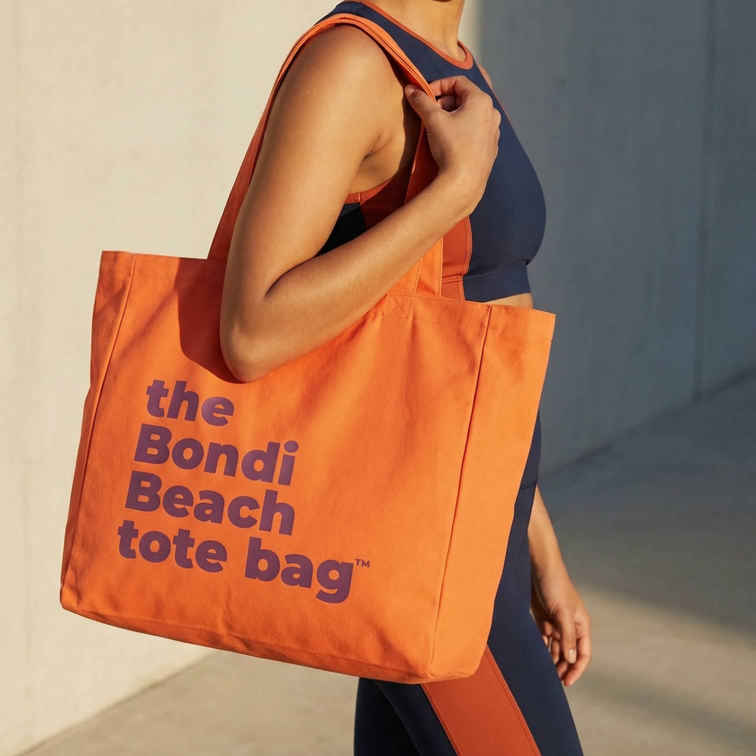 Person holding an orange tote bag with 'the Bondi Beach tote bag' text.