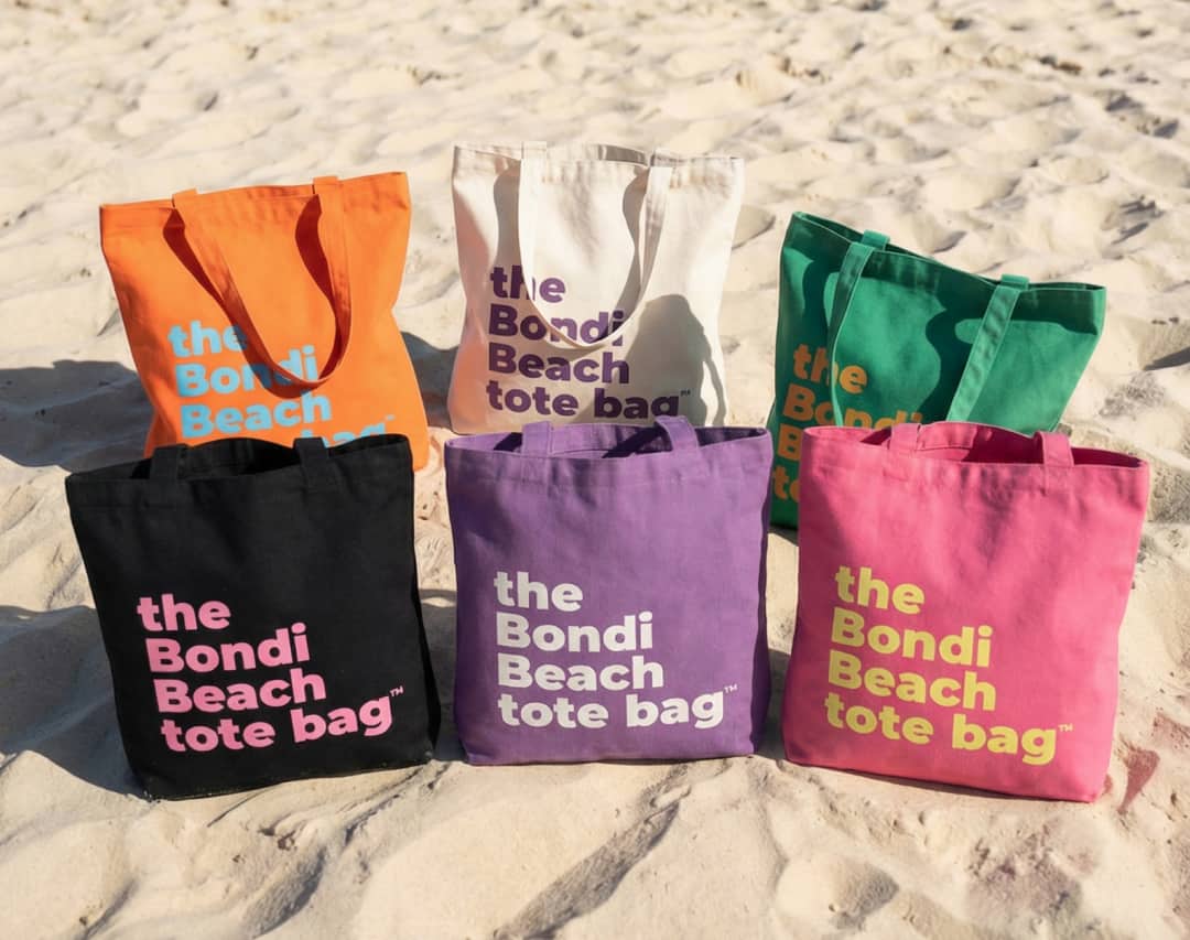 Set of colourful canvas Bondi Beach tote bags displayed on sandy background.
